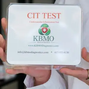 A hand holds a CIT TEST box labeled KBMO with contact details.