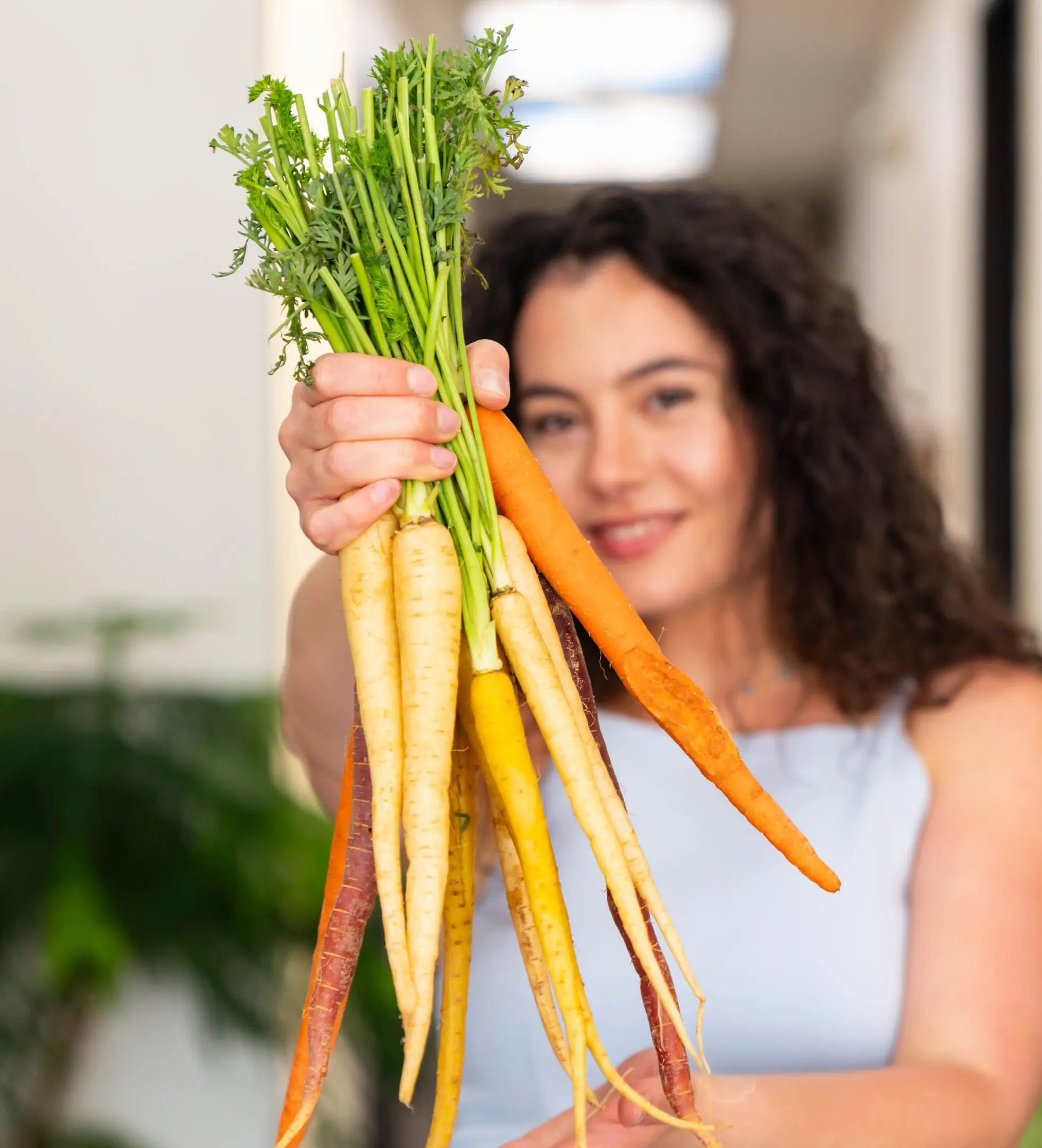 Woman holding a bunch of fresh yellow and orange carrots.