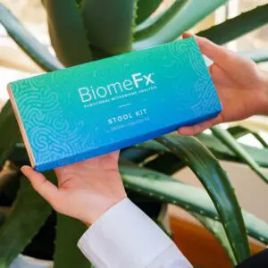 Hands holding a BiomeFx supplement box with green plants in the background.