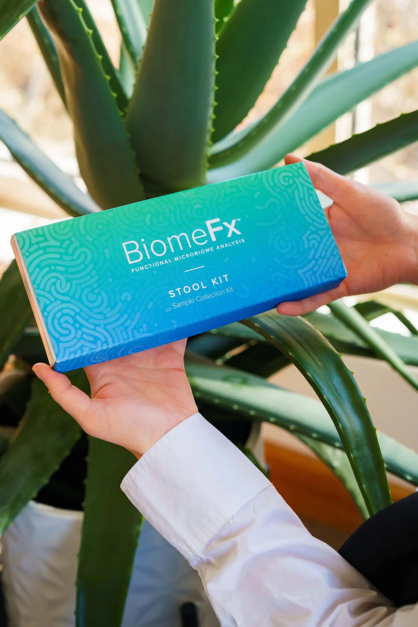 Hands holding a BiomeFx supplement box with green plants in the background.