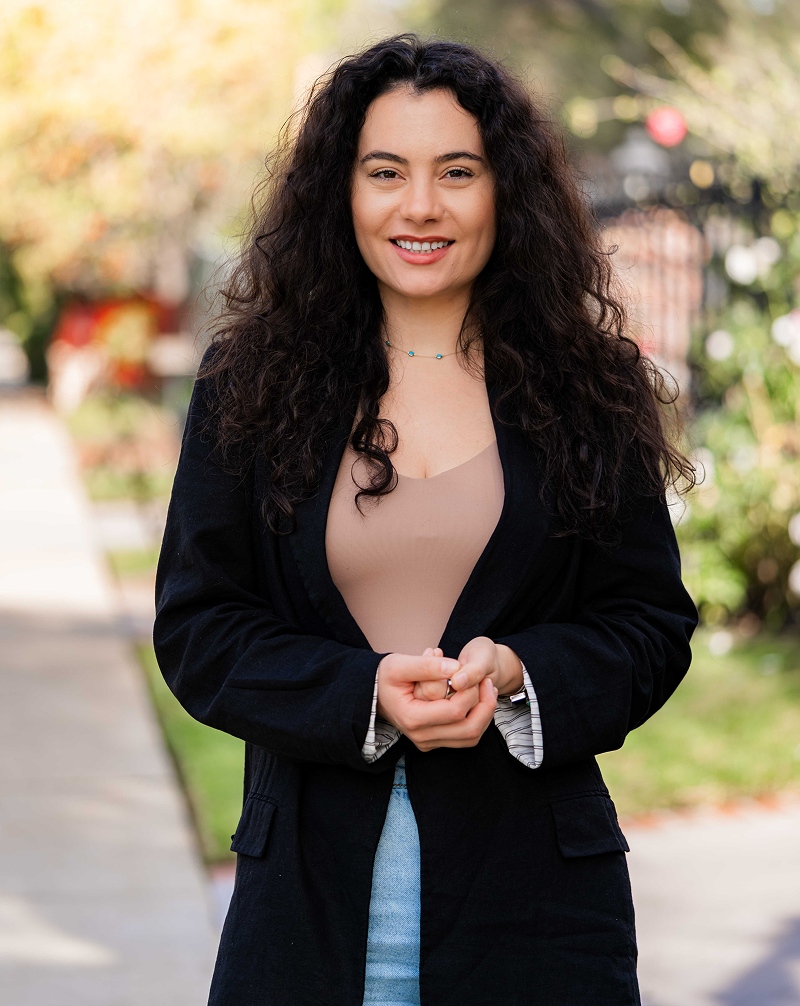 Smiling woman with long curly hair standing outdoors in casual attire.